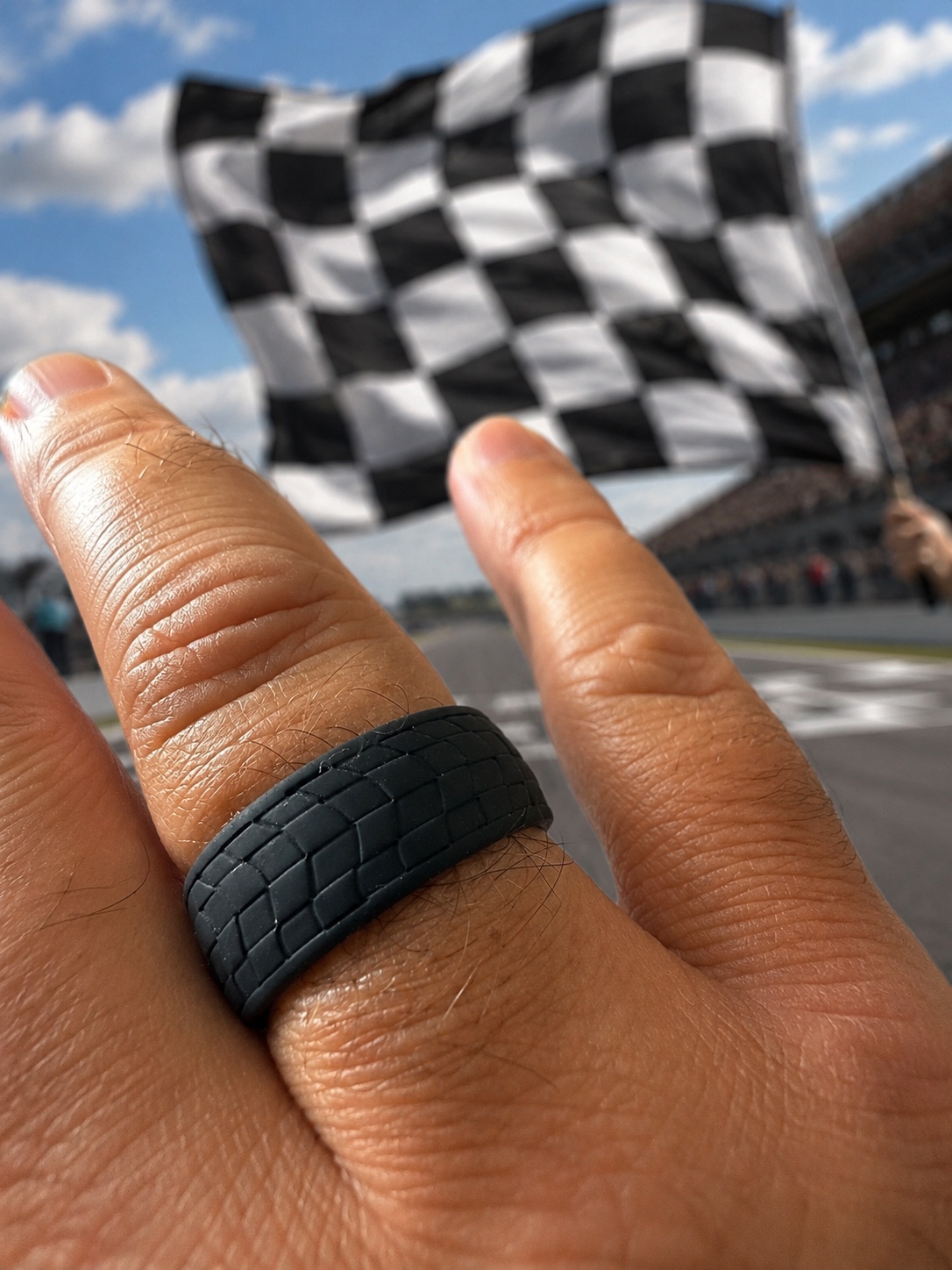Black motorsport silicone ring worn at a racing circuit beneath a chequered flag